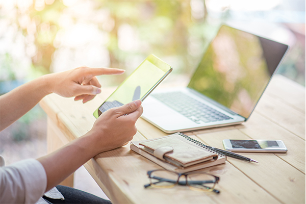 Person using tablet with mobile phone and laptop in the table