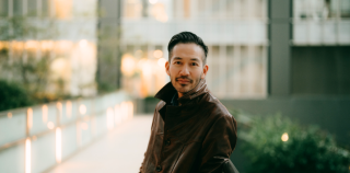 Image of a smiling Asian man standing in front of a building.